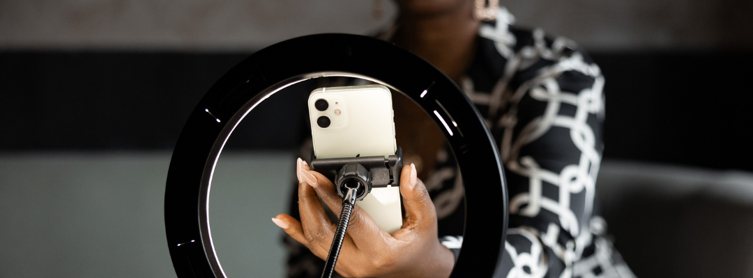 A woman's hand holding a phone and a ring light