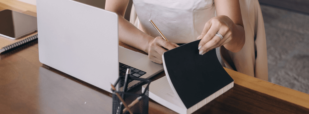 Writing in a notebook with a laptop next to the notebook