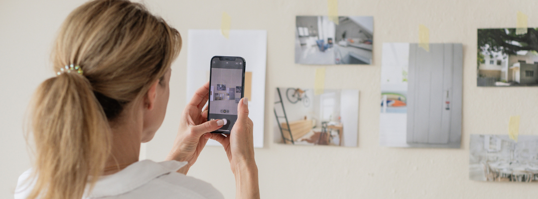 A woman taking a picture with her iphone of a wall with images taped to it