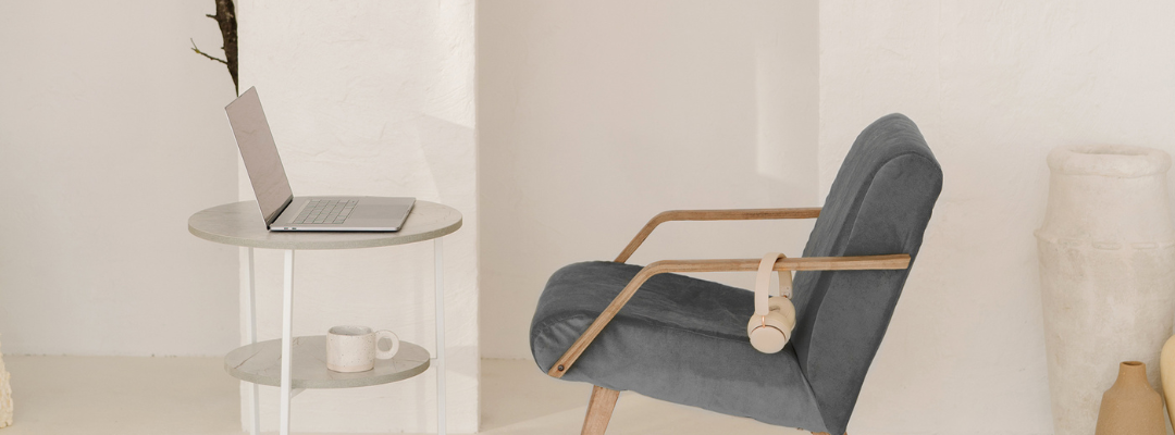 A gray chair with headphones hanging off the arm rest. Chair in front of table with open laptop.
